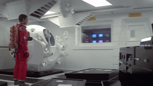 This gif depicts David Bowman walking towards HAL9000. He places his hand on the unit that the AI is attached to, and leans forward while reaching his hand out towards one of Hal's red fisheye lenses, almost like if he's about to caress him.